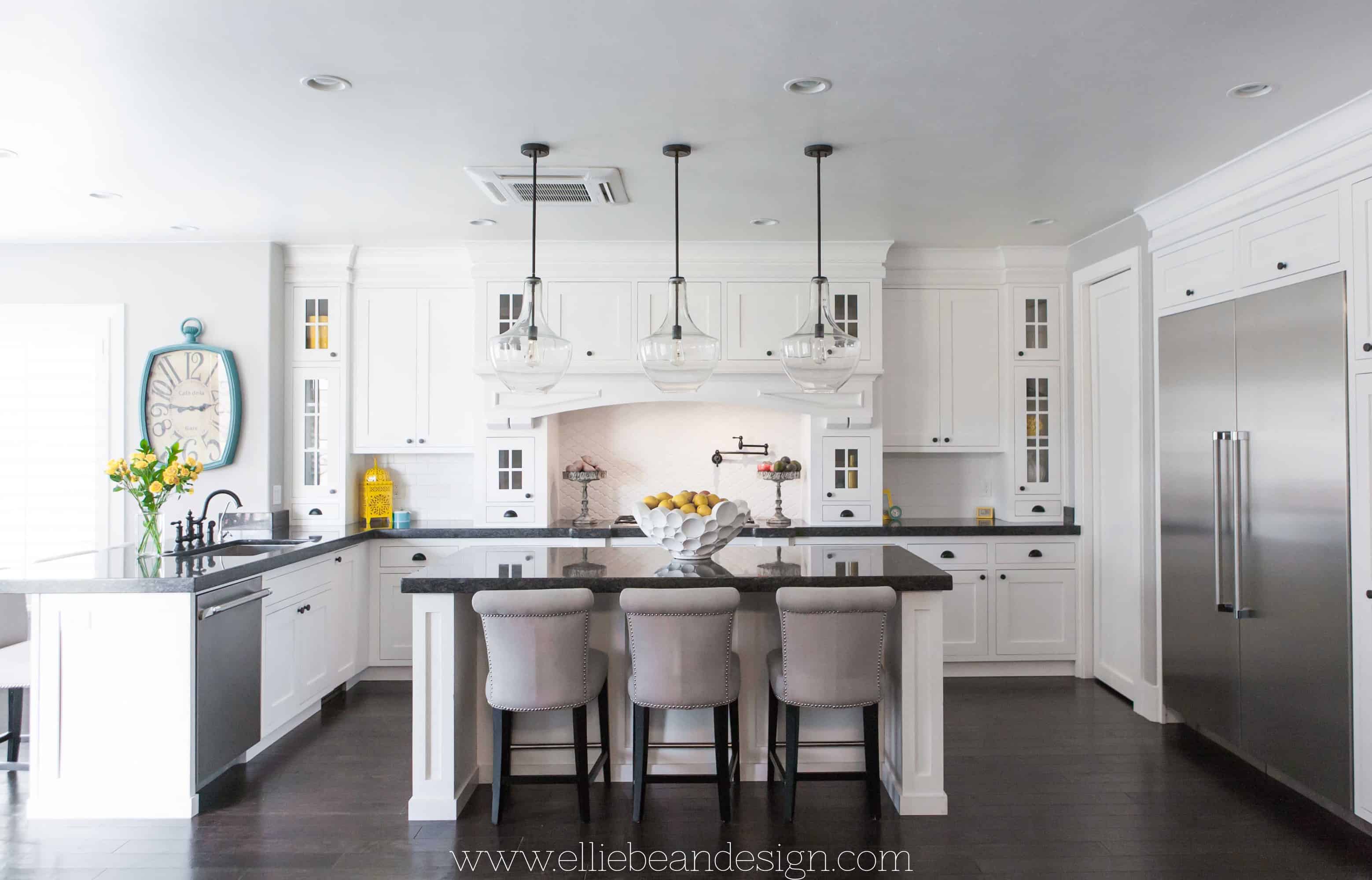 A gorgeous white kitchen, with a large kitchen island with 3 large pendents hanging over the top!